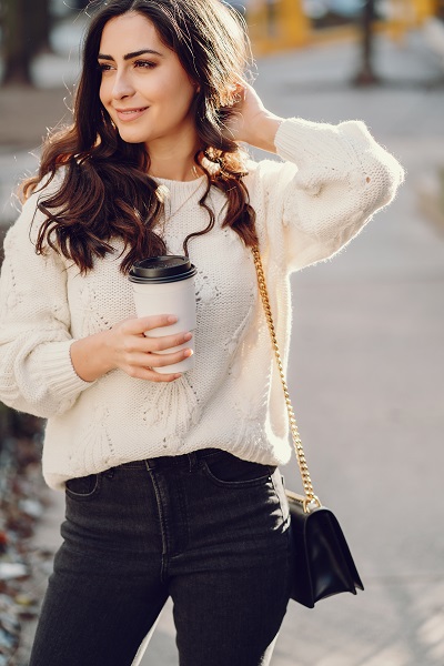 Cute Ukrainian brunette in a white sweater holding her cup of coffee posing in a city
