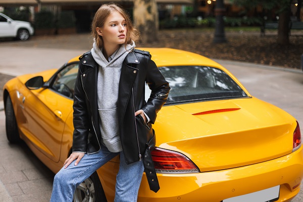 Young beautiful Ukrainian woman in a leather jacket leaning on a yellow sport car