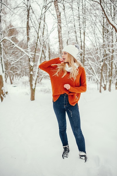 Young beautiful Ukrainian girl in a cute orange sweater standing in a snowy forest alone