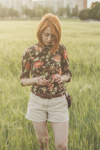 Attractive Ukrainian woman posing on a green field with a city on a background standing alone