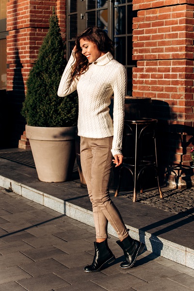 Stylish Ukrainian girl dressed in a white knitted sweater and light pants poses in the street