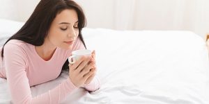 Young attractive Ukrainian woman smelling her aromatic coffee in a bed with her closed eyes