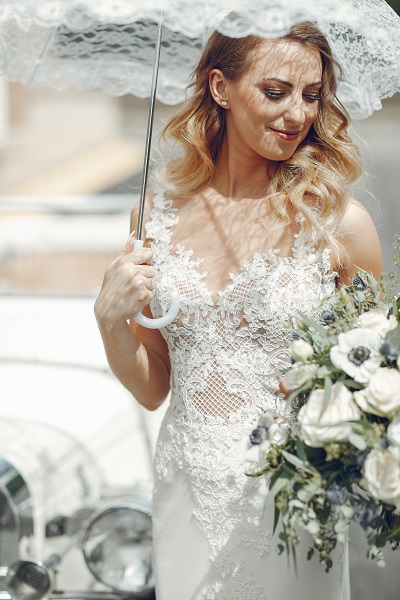 Elegant young Ukrainian bride holding a bouquet of white flowers in one hand and an umbrella in another one