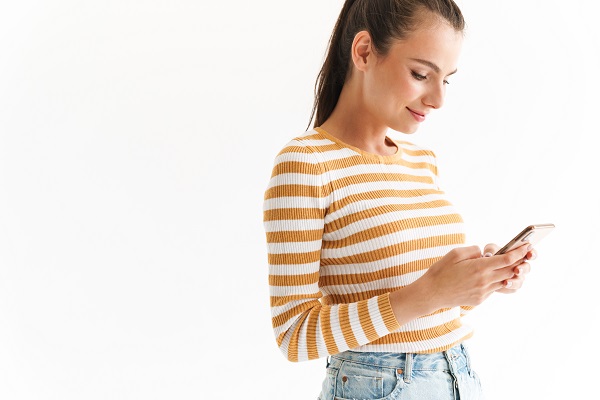 Smiling young Ukrainian girl wearing casual clothing using her mobile phone on a white background